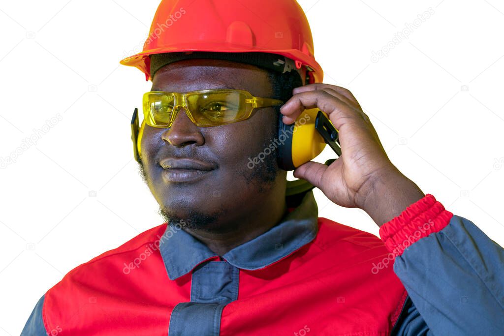 Portrait Of Black Industrial Worker In Personal Protective Equipment Isolated On White Background. Young African American Worker In Red Helmet, Hearing Protection Equipment And Work Uniform.
