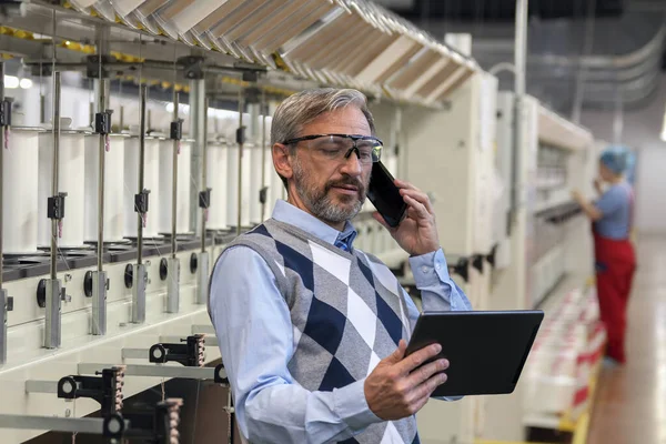 在纺织厂 成熟的经理看着数字制表屏风和电话的使用 灰白头发的商人的形象 使用智能电话及数码记事板的人 — 图库照片