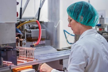 İlaç Endüstrisi Üretim Hattı İşçisi. İlaç fabrikasındaki ambalaj hattında robotik kol kaldırma ampulleri. İlaç Üretimi.