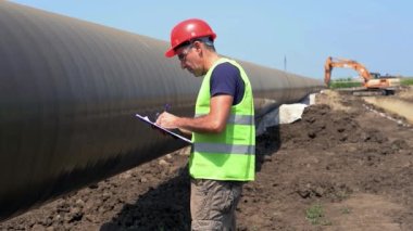 Doğal Gaz Boru Hattı İnşaat Alanında Kırmızı Hardhat Giyen İnşaat Ustabaşı. Yavaş Hareket. Gaz Borularının Yanında Yürüyen İşçi. Türk Akımı Boru Hattı İnşaatı.