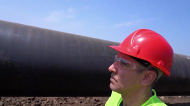 İnşaat Ustabaşının Kırmızı Kazaklı Doğal Gaz Boru Hattı İnşaat Alanında Yürüme Yakın Çekimi - Yavaş Hareket. İş Başlığı ve Yağ ya da Gaz Borusu Yanındaki Sarı Yelek Portresi.