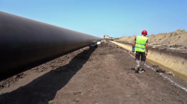 İnşaat Denetmeni Doğal Gaz Boru Hattı İnşaat Alanında Yavaş Çekimde Yürüyor. İnşaat alanındaki Petrokimya Petrol ya da Gaz Boru Hattı 'nı kontrol eden Hardhat İşçisi. Boru Hattı İnşaat Altında.