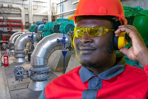 非洲裔美国工人在工业室内用管道和发电机进行保护工作的肖像 红头盔 护目镜 听觉保护装置及工作服工人 — 图库照片