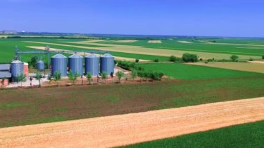 Tarımsal tarımsal alanda tahıl ambarlarının üzerinde uçuyor. Yazın mavi gökyüzü altında tahıl ambarlarıyla bereketli düzlüklerin panoramik manzarası.