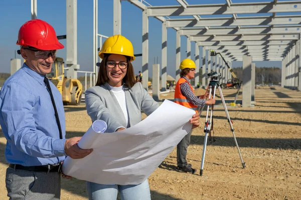 Smiling Female Architect Supervisor Checking Blueprint Future Factory Construction Site lizenzfreie Stockbilder