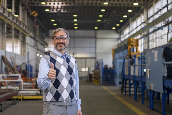 Smiling Production Manager Standing In Factory Hall And Giving Thumb Up. Portrait Of Confident, Handsome, Gray-Haired Businessman In Industrial Interior.