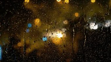 Gece Melankoli - Yağmurda Şehir. Bulanık Şehir Gecesi Aydınlatması 'nın Yağmur Damlalarıyla Pencereye Bakışı. Şehir ışıkları ve trafik Yağmurlu bir gecede.