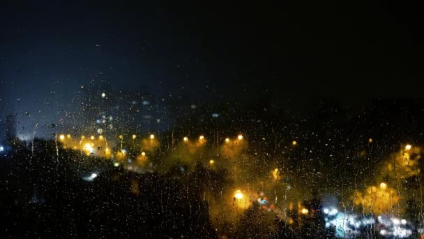 雷雨の間 夜の街の通りに対して窓に雨が降ります 雨が降る窓からの都市の夜の照明の景色 雨の夜の街の光と交通 憂鬱の雨 — ストック動画