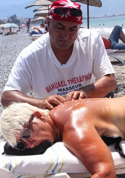 Массажист делает полный массаж красивой женщине на пляже — стоковое фото
