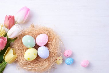 Mutlu Paskalya yumurtaları yuvada ve çiçekler ahşap arka planda fotokopi alanı ile.