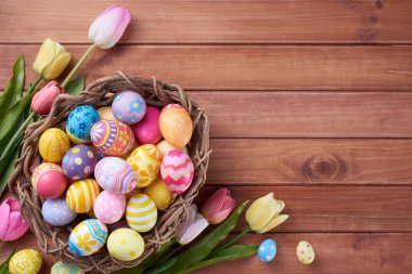 Mutlu Paskalya yumurtaları yuvada ve çiçekler ahşap arka planda fotokopi alanı ile.