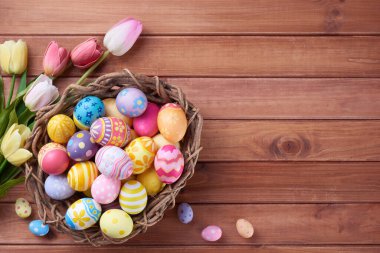 Mutlu Paskalya yumurtaları yuvada ve çiçekler ahşap arka planda fotokopi alanı ile.