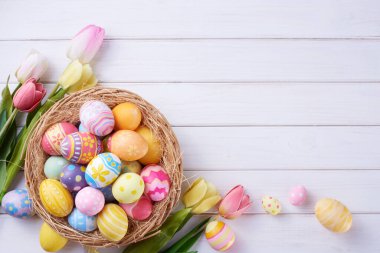 Mutlu Paskalya yumurtaları sepette ve çiçekler ahşap arka planda fotokopi alanı ile.