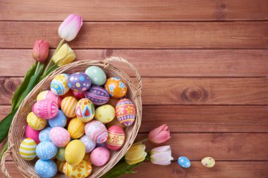Mutlu Paskalya yumurtaları sepette ve çiçekler ahşap arka planda fotokopi alanı ile.