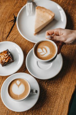 Woman is holding a cup of coffee near cheesecake and brownie pla