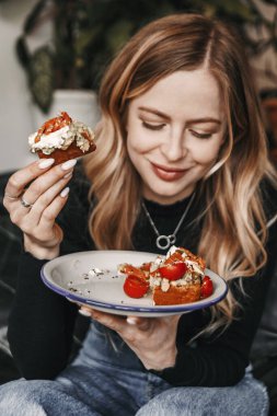 Young blonde woman is eating avocado toast for breakfast in a ca