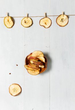 Elma cipsi Sağlıklı, organik atıştırmalıklar. Bir ipe asılı kurumuş elma dilimleri ve cips ile ahşap bir kase. Gri ahşap arkaplanda düz bir alan