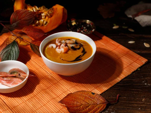 Sopa de crema de calabaza con camarones y crema balsámica. En una servilleta de bambú naranja con hojas brillantes de otoño. Tecla baja. — Foto de Stock