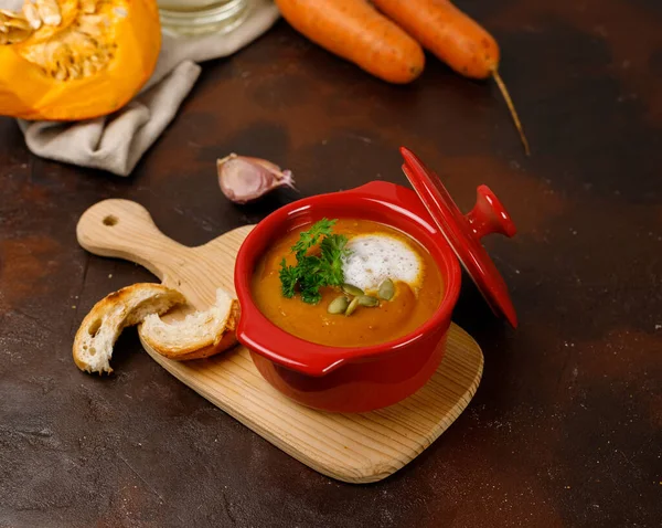 Seramik kırmızı kasede kalın balkabağı çorbası. Hafif ahşap bir masada, içinde yemek malzemeleri var. Yakın plan, boşluğun kopyası