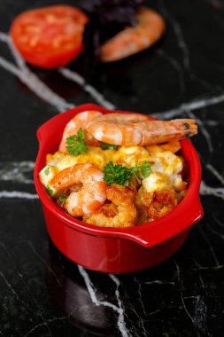 Garides Saganaki. Sıcak Yunan aperatifi, sebze ve peynirli Girit karidesi, siyah mermer arka planda, koyu gölgeli. Yakın plan, seçici çerçeve, dikey çerçeve.