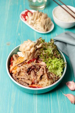 Chapche, kızarmış sığır eti, istiridye mantarı ve sebzeli funchosa. Kore kuni 'sinin ulusal bayram yemeği. Mavi tahta bir masaya yakın plan, dikey.