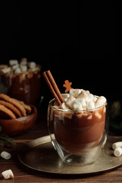 Heißer Kakao mit Marshmallows und Zimt im Glas, auf einem runden Kupferblech, im Hintergrund Plätzchen und Tannenzweige. — Stockfoto