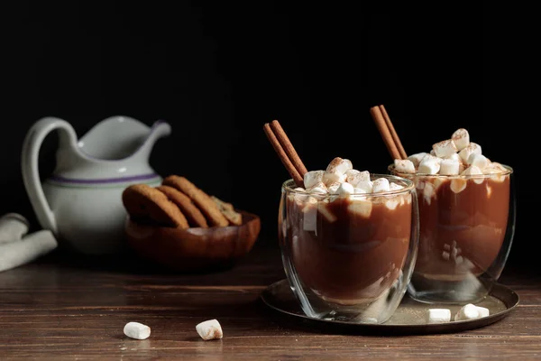 Zwei Thermosbecher mit heißer Schokolade, Kakao und irischem Kaffee mit Marshmallows. Auf dunklem Hintergrund, horizontal, Kekse und Sahne in einer Kanne im Hintergrund — Stockfoto