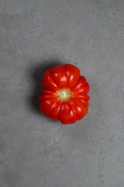 Gri arka planda, yakın planda, olgun, kırmızı flütlü bir domates. Düz Yatay.