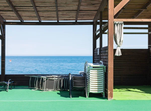 Un hotel o una playa de la ciudad en la orilla del mar antes del comienzo o al final de la temporada. una pila de tumbonas, un café de verano vacío —  Fotos de Stock