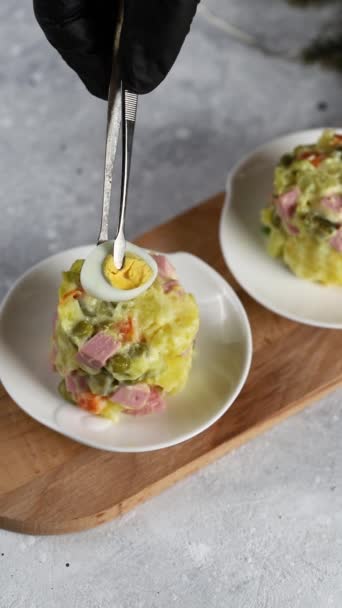 Estilo de comida. Un chef con guantes decora una porción de ensalada con perejil y medio huevo de codorniz, usando pinzas. Vertical — Vídeos de Stock