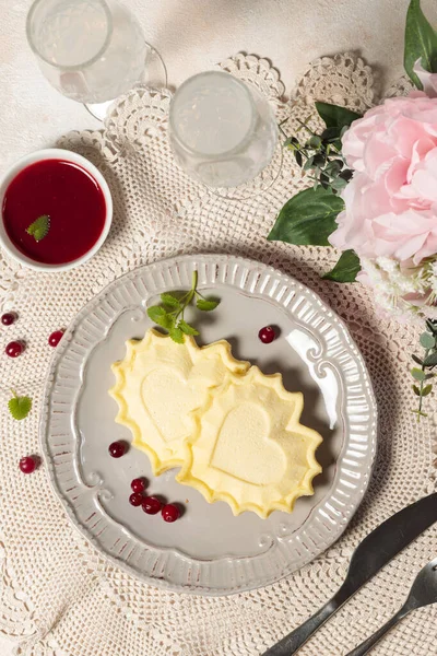 Pfannkuchen, Kekse oder Käsekuchen in Herzform auf einem Teller. Auf einer Spitzenserviette mit Champagnergläsern und Blumen. — Stockfoto