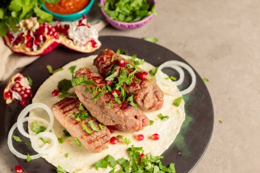  İnce pide ekmekli kebaplar, otlar, soğanlar ve nar tohumlarıyla. Baharatlı domates sosu, bitkiler ve nar..