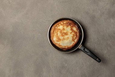 Kızartma tavasında bir yığın ince krep. Gri arkaplanda en üstteki görünüm, boşluğun bir kopyası