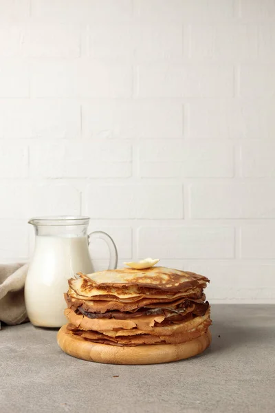 A stack of thin pancakes on a wooden plate and a jug of milk. Close-up, vertical, copy of the space — Stock Photo, Image