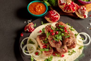 Et sosisi, otlu lula kebabı, soğan, domates sosu ve nar. Siyah arkaplanda, yatay olarak yakın plan