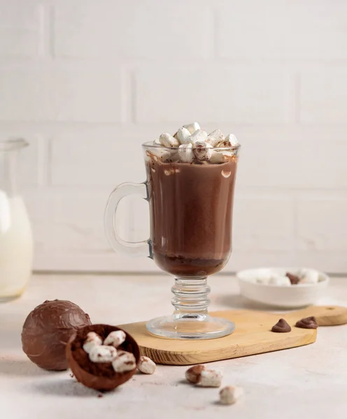 Kakao oder heiße Schokolade in einem hohen Glasbecher und eine Schokoladenbombe mit einem Mini-Marshmallow zum Zubereiten eines Getränks. Nahaufnahme, selektiver Fokus — Stockfoto
