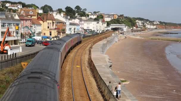 Train travelling away from camera viewed from bridge on railway bordering sand and sea Dawlish Devon England — Stock Video