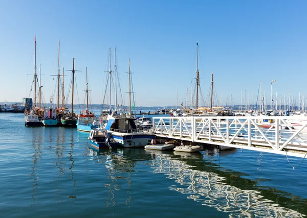 Pasarela de embarcadero blanco que conduce a barcos y yates en un puerto deportivo con cielo azul y reflejos — Foto de Stock