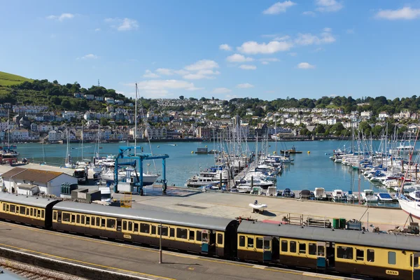 Dartmouth och Kingswear tågstation med färgglada gula vagnar på järnvägsspår genom marina med båtar med blå himmel och moln i Devon England Uk — Stockfoto