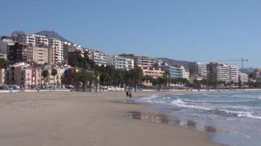 Palmiye ağaçları, dalgalar ve Costa Blanca Alicante 'de yürüyen uzak çiftli Villajoyosa İspanya plajı.