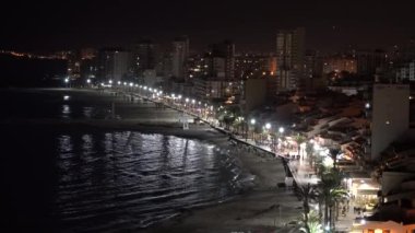 Gece vakti El Campello Costa Blanca kıyı kasabası İspanya Parlak ışıkları, palmiye ağaçları, deniz ve gece vakti uzak insanlar