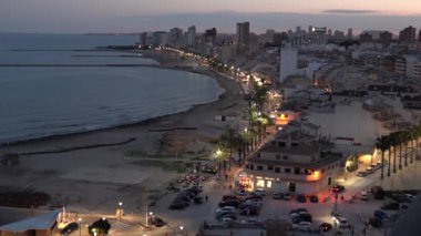 Akşamın erken saatlerinde İspanya 'nın El Campello' sunda gece olmadan önce uzaktaki insanlar, ışıklar açık, palmiye ağaçları ve deniz vardı.