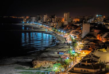 İspanya 'nın El Campello, Alicante kentinde 9 Nisan 2022' de parlak ışıklar, palmiye ağaçları ve denizle gece vaktidir.