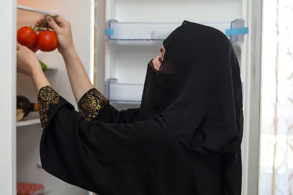 民族衣装を着たイスラム教徒の女性が新しい空の冷蔵庫で赤いジューシーなトマトを産む — ストック写真