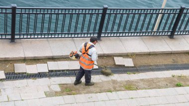 İşçi, yıkılmış nehir setinin çimlerini biçiyor..