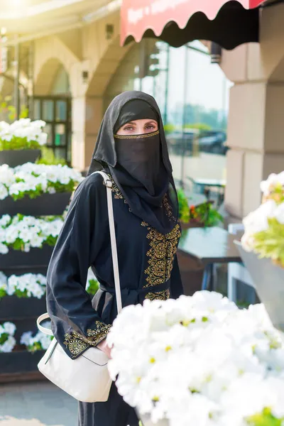 一位穿着民族服装的年轻穆斯林妇女在街上美丽的白花中的画像 — 图库照片