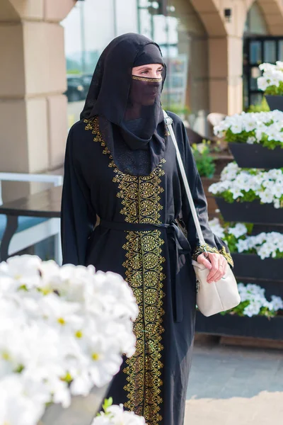 一位穿着民族服装的年轻穆斯林妇女在美丽的白花中的画像 — 图库照片
