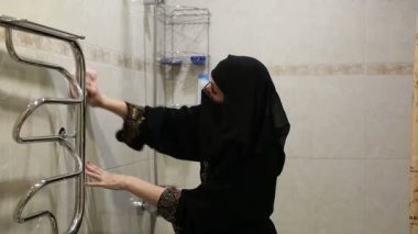 Banyoda ulusal kıyafetleri olan Müslüman bir kadın işleri yoluna koyar, bir borudan, bir bataryadan ve ısıtılmış bir havludan toz temizler..