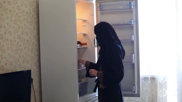 新しい空の冷蔵庫の近くの台所にイスラム教徒の女性が立っている — ストック動画