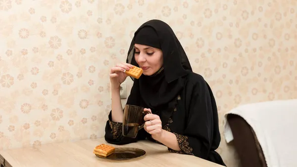 民族衣装を着たイスラム教徒の女性はキッチンテーブルでお茶とクッキーと朝食を持っています — ストック写真